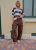 Person wearing a striped sweater and brown pants standing on a brick sidewalk.