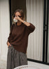 Woman in a brown sweater and striped skirt holding a white mug, standing in front of a mirror.