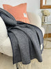 Gray throw blanket draped over a chair with an orange pillow in a cozy living room setting.