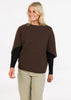 Woman wearing a brown poncho over a black top and beige pants on a white background