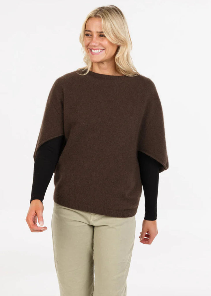 Woman wearing a brown poncho over a black top and beige pants on a white background