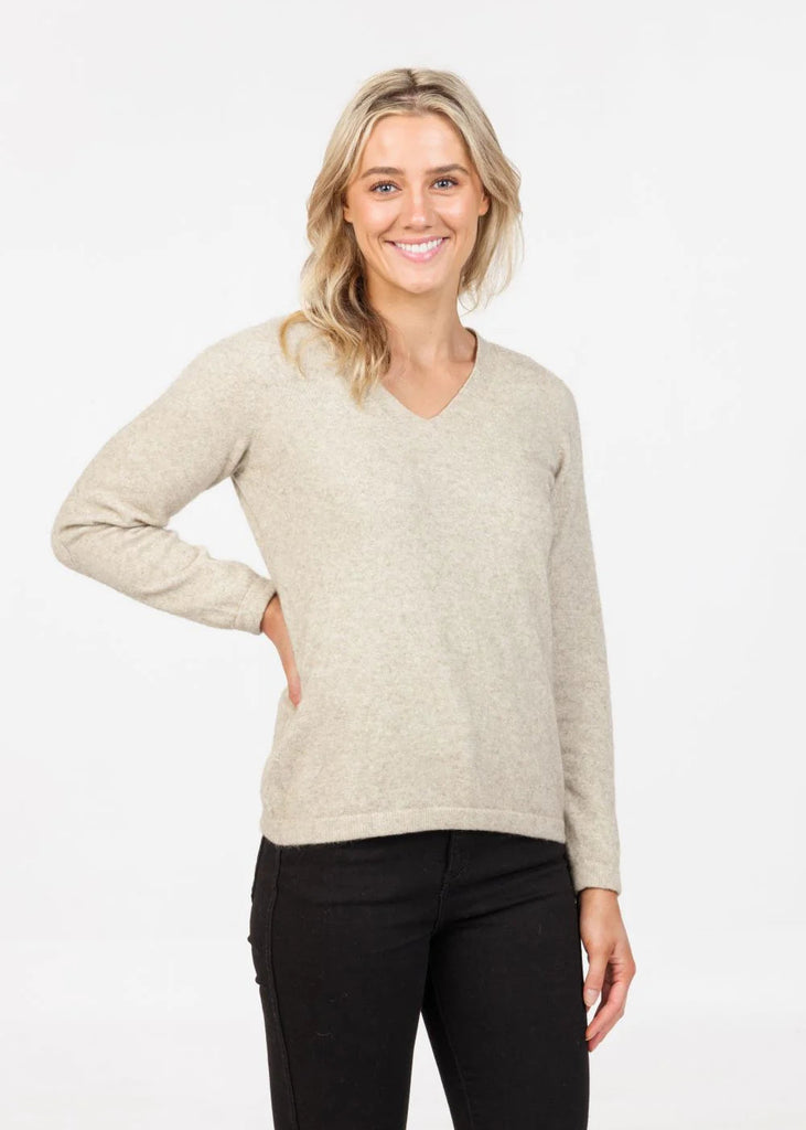 Woman wearing a beige sweater and black pants on a white background