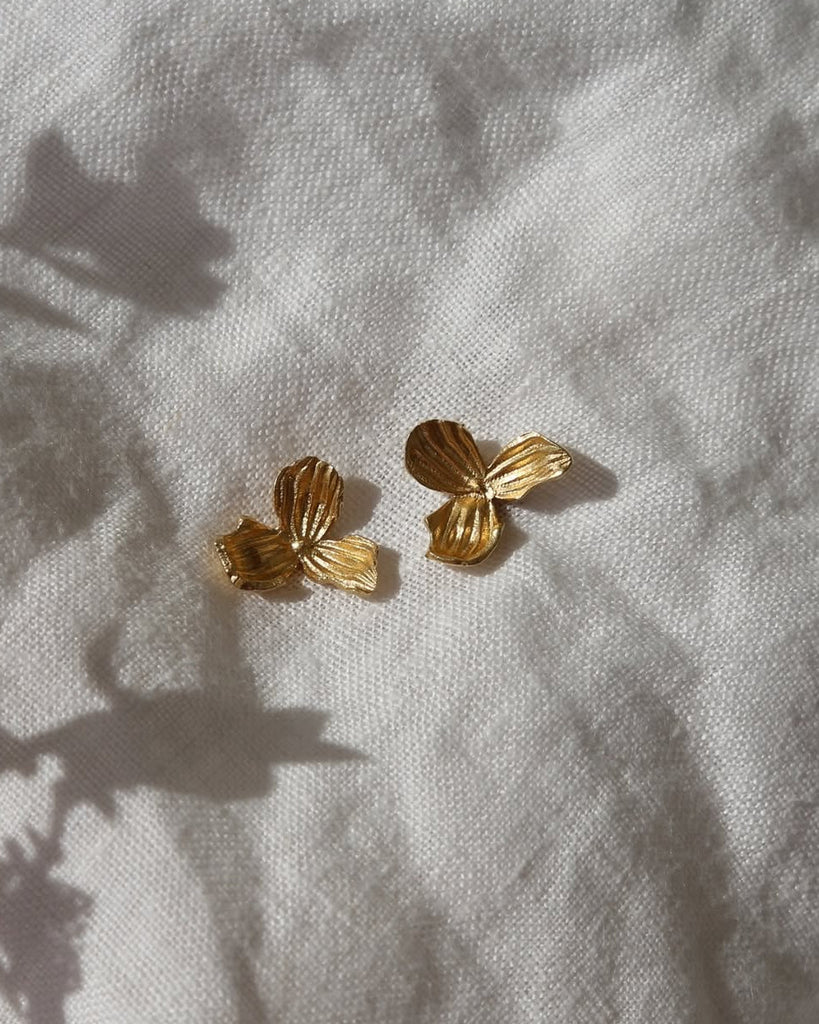 Gold butterfly-shaped earrings on a textured light fabric background